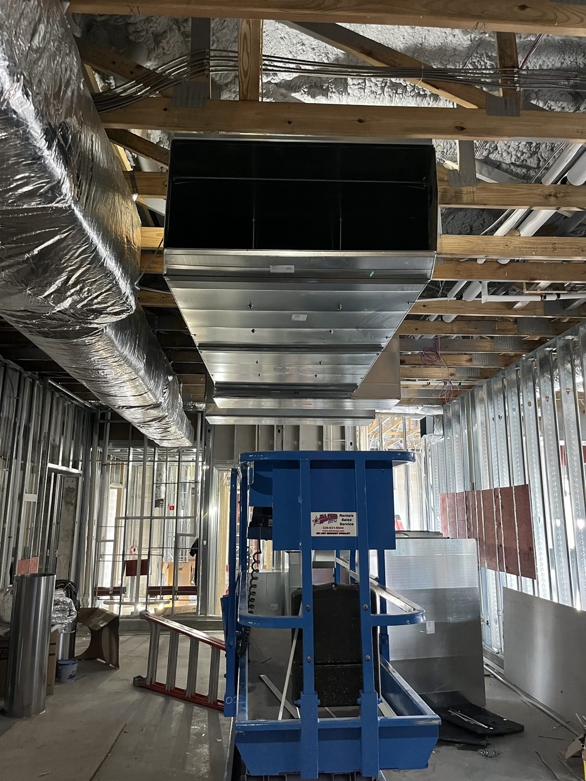 A return main on a lift. Commercial buildout, before the ceiling closes.